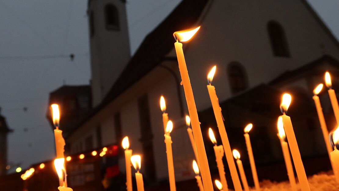 Schmale, brennende Kerzen vor der abendlichen Kulisse der Luzerner Peterskapelle